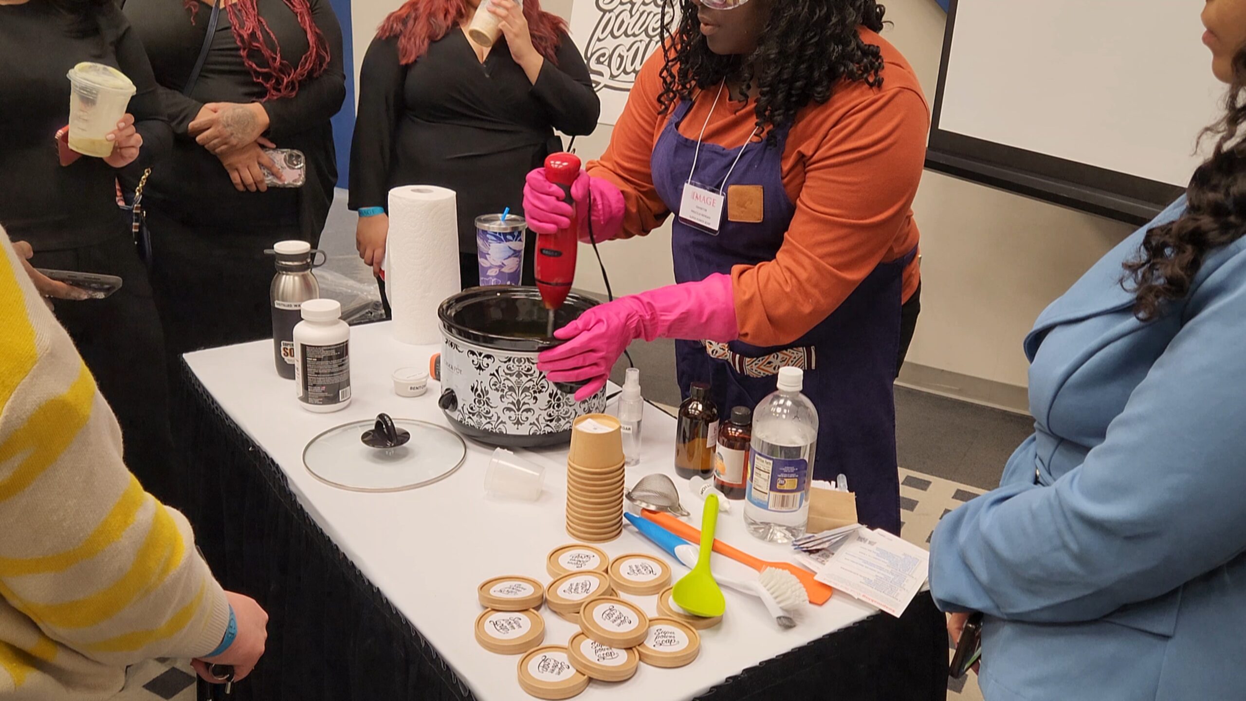 Super Power Soap - houston soapmaking classes Group of diverse conference attendees gathered around a live soapmaking demonstration led by the founder of Super Power Soap, showcasing hands-on learning, creativity, and engagement at The Image Expo - October 2024.