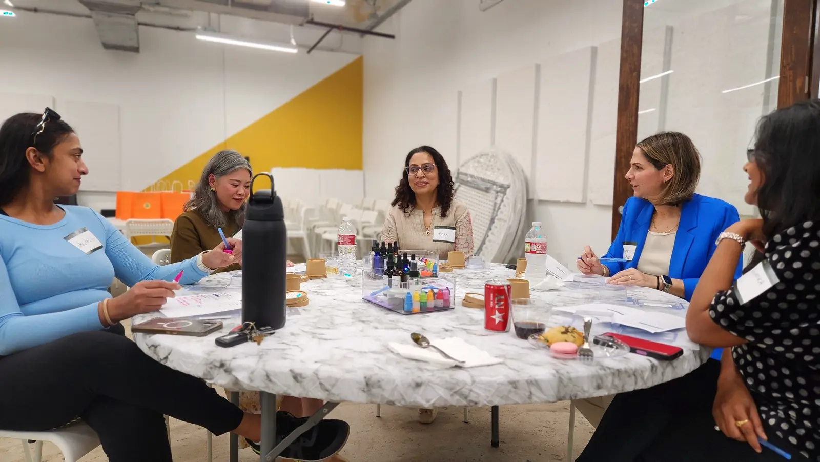Evidence Image: Conversation develops around a shared task instead of a forced icebreaker. Houston colleagues talking around a table during a guided soapmaking workshop